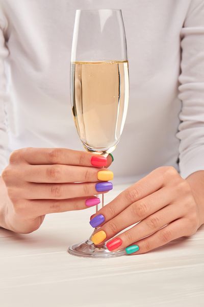 Hands with rainbow painted nails holding a flute of bubbles
