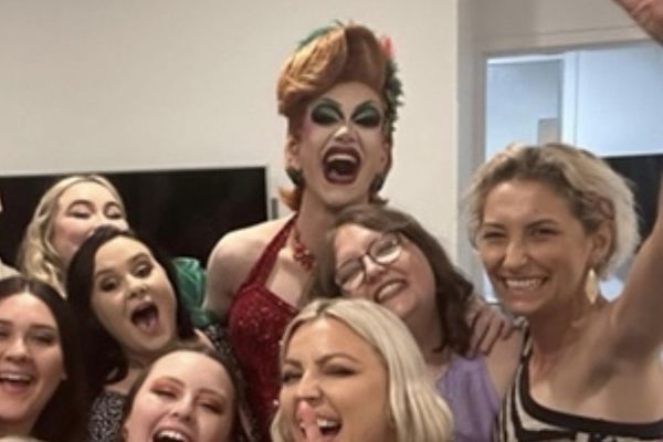 A drag queen and a group of laughing friends crowding in for a selfie
