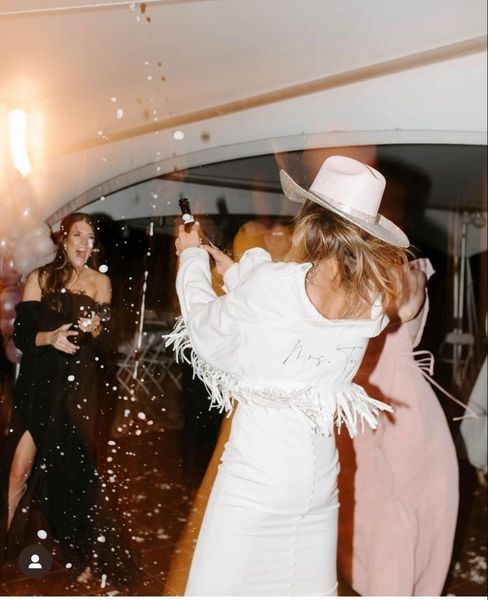 A bride to be in a white cowboy hat and fringed jacket popping bubbles with friends