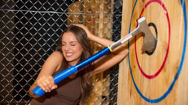 A laughing woman throwing an axe at a wooden target