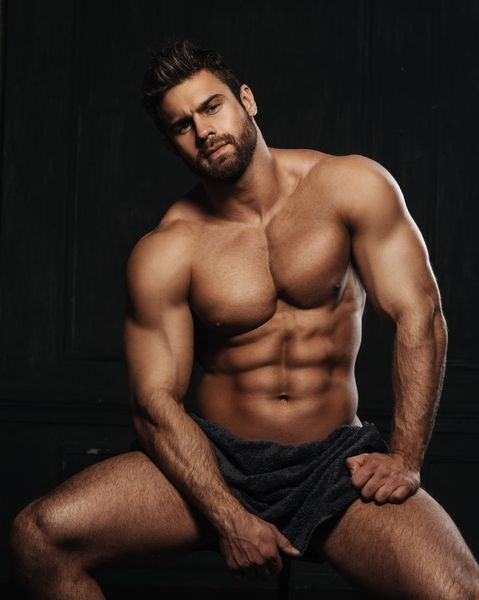 A shirtless male model seated against a dark background