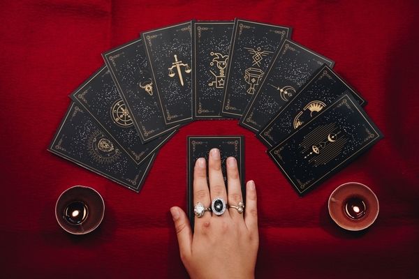 A hand with silver rings resting on a spread of black tarot cards between candles