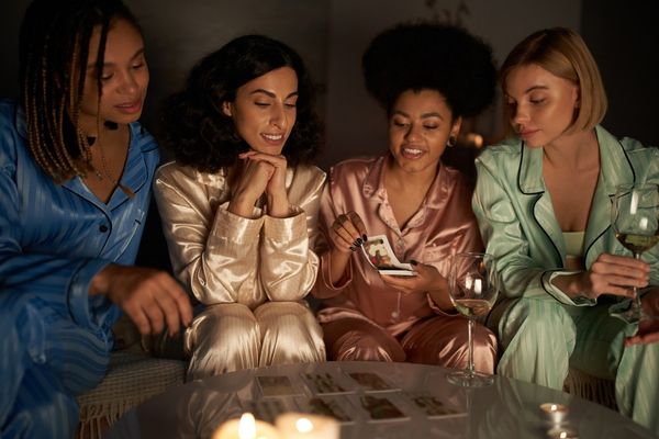 Four women in silk pyjamas leaning in over tarot cards laid out by candlelight