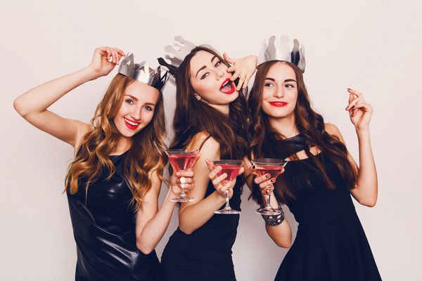 Three lovely ladies dressed in elegant black dresses and silver crowns smile and pose in a group photo with champagne glasses in their hands