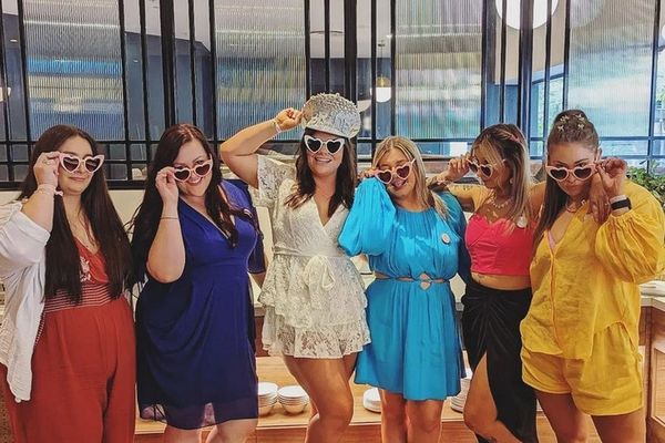 Six friends in bright outfits striking poses in heart sunglasses in a restaurant