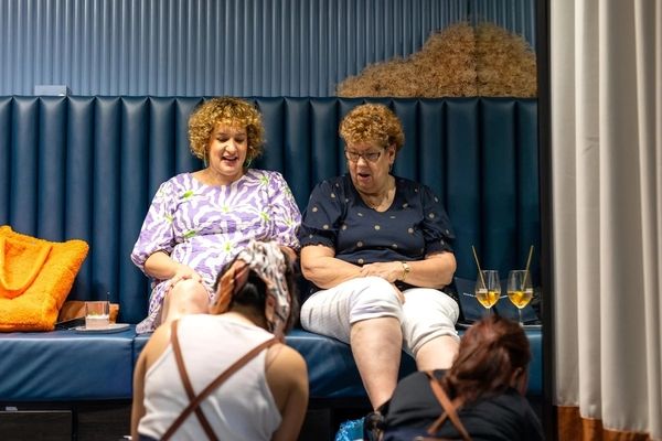 Two friends laughing over bubbly in a velvet booth while their pedicures are done