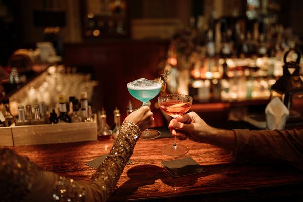 Two hands raising colourful cocktails at a candlelit bar