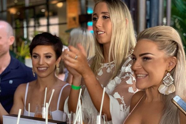 Four friends laughing around a table at a busy riverside bar