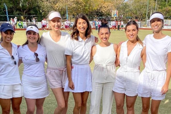 Eight women dressed in white standing arm in arm on a lawn bowls green