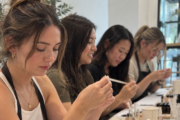 Friends in aprons test perfume oils with scent strips along a long table