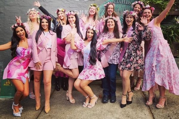 A hens group in pink with flower crowns and sashes cheering together outside