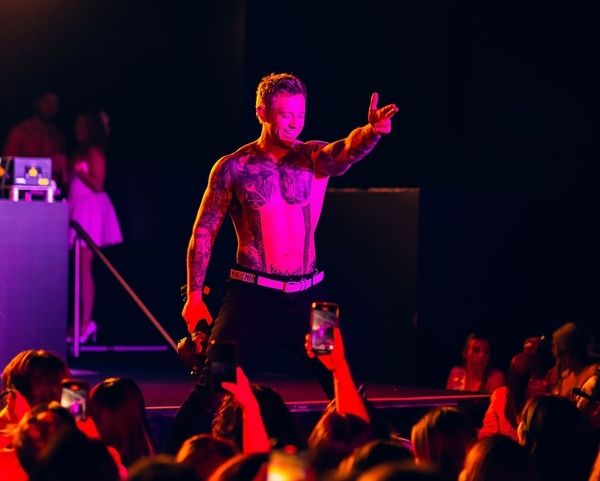 A shirtless performer on stage as a crowd films him on their phones