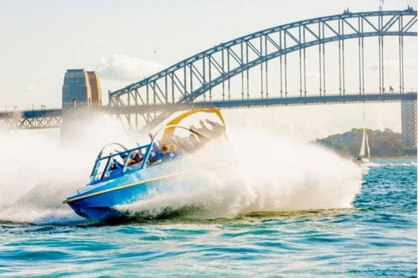 Blue jet boat full of riders spinning through spray below the Sydney Harbour Bridge
