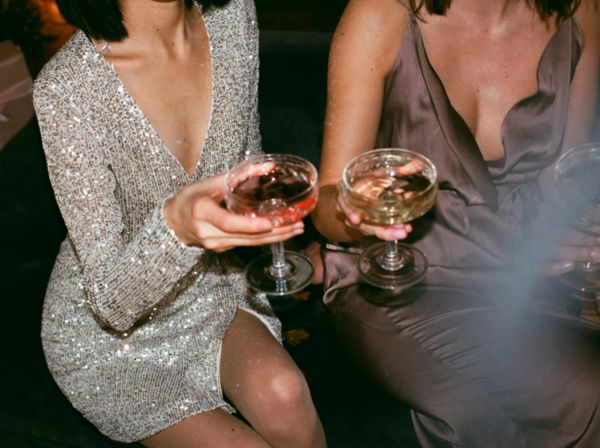 Two friends in sequin and satin dresses holding coupes of pink bubbles