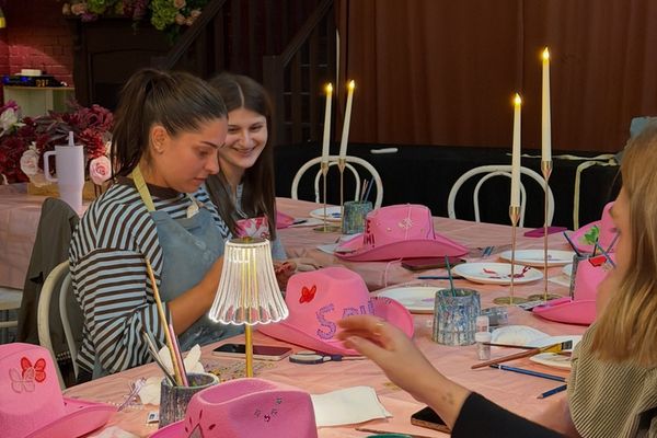 Friends decorate pink cowboy hats at a candlelit table in a private room