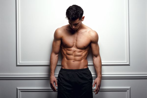 male model with washboard abs standing in front of white wall posing