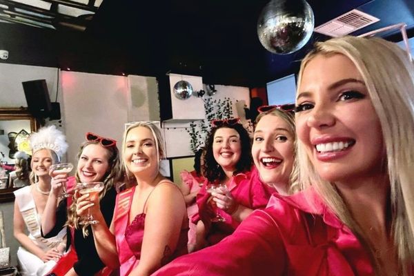 Friends in pink crowd into a laughing selfie under a disco ball