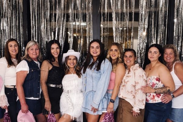 A cowgirl hens group of all ages with the bride in a white hat before silver tinsel