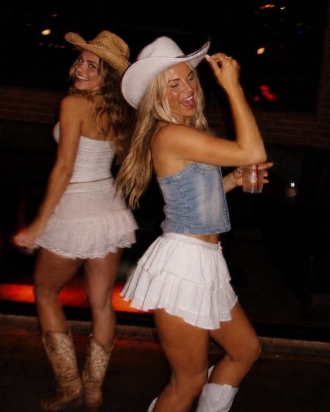 Two friends in cowboy hats and white skirts dancing