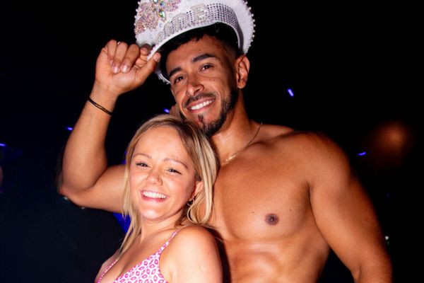 Hen in pink laughing with a shirtless waiter wearing her sparkly Bride hat