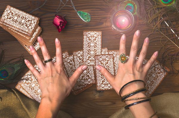 Hands in rings and bangles laying tarot cards on a wooden table beside a candle