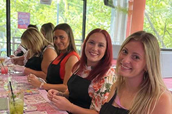 Smiling friends in aprons sit along a table of beads and gold charms