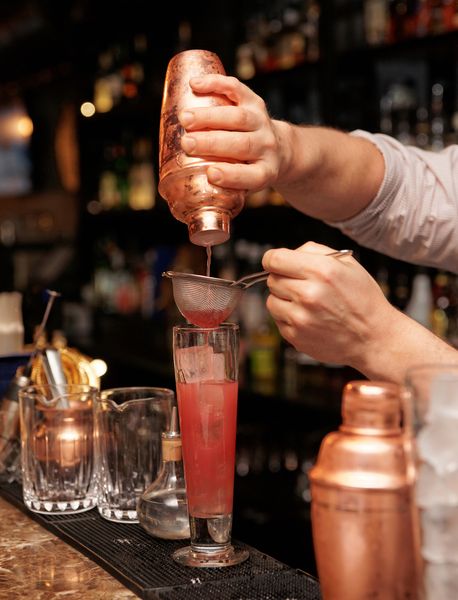 expert mixologist pouring cocktails into a glass at the bar