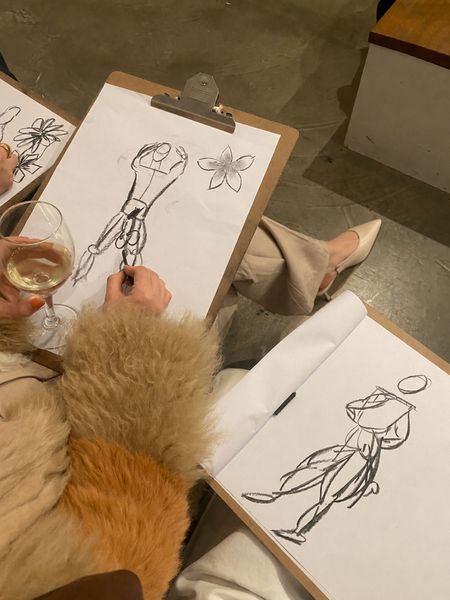 Life drawing sketches on clipboards beside a glass of white wine