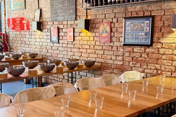 A brick walled class room with mixing bowls, long timber tables and wine shelves