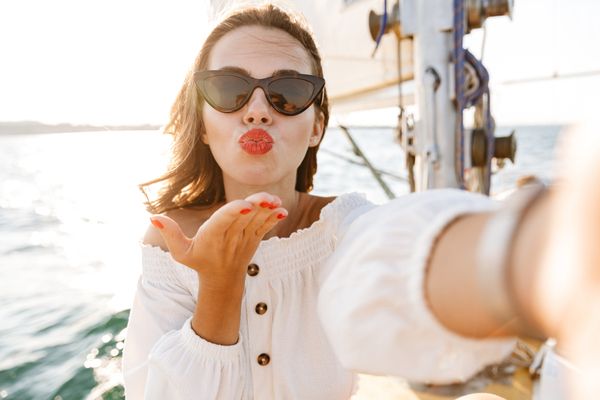 A woman in cat-eye sunglasses blowing a kiss on a yacht