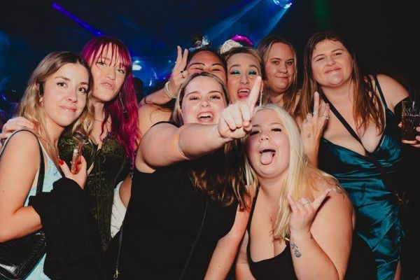 Group of friends laughing and posing for a selfie inside a colourful late-night venue