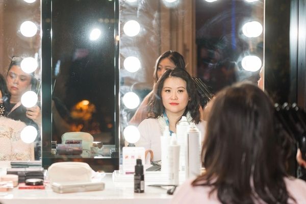 Guests watch their makeovers in lit makeup mirrors while artists work behind them