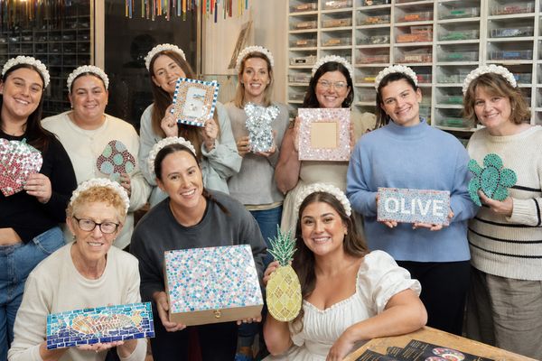 Hens group in matching headbands holding their mosaics, one spelling OLIVE, bride seated front