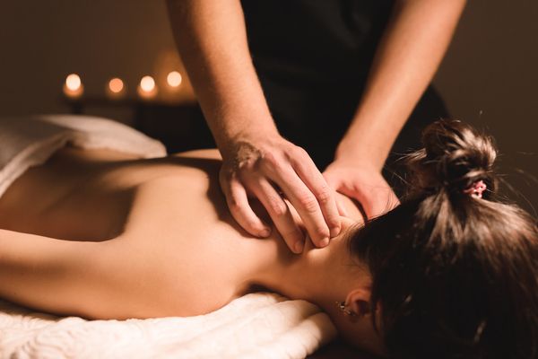 A therapist giving a woman a neck and shoulder massage by candlelight