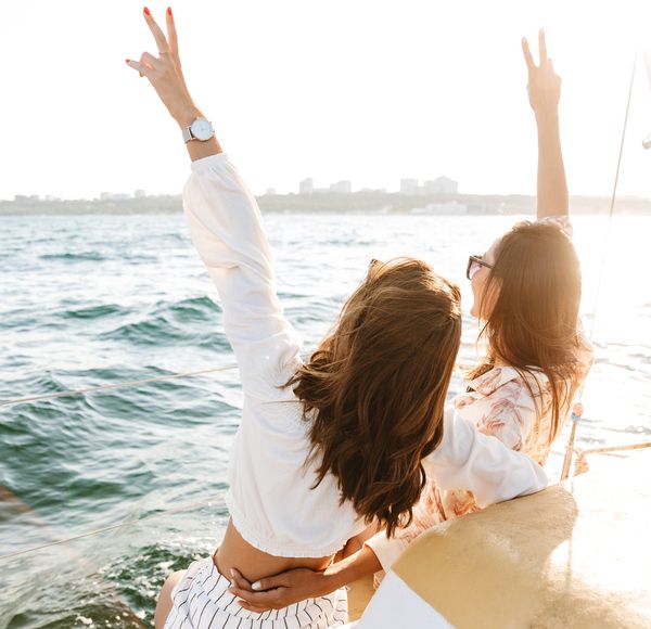 Two friends with their arms in the air at the front of a boat on the water