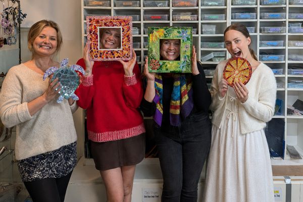 Four friends laughing, two peeking through the mosaic frames they just made