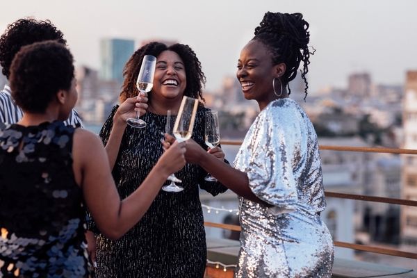 three woment standing on rooftop bar sipping bubbly and laughing