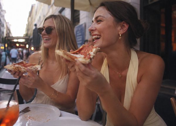 Two friends laughing as they share pizza at an outdoor table