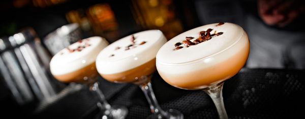 three espresso martinis lined up on the bar sprinkled with coffee beans on top