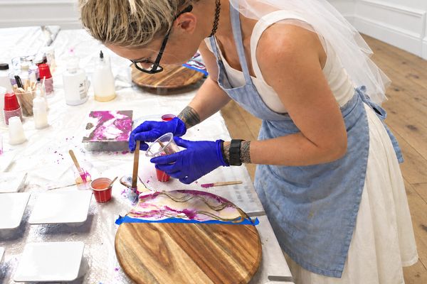 The bride in her veil and apron pouring gold and pink resin onto a round wooden cheeseboard