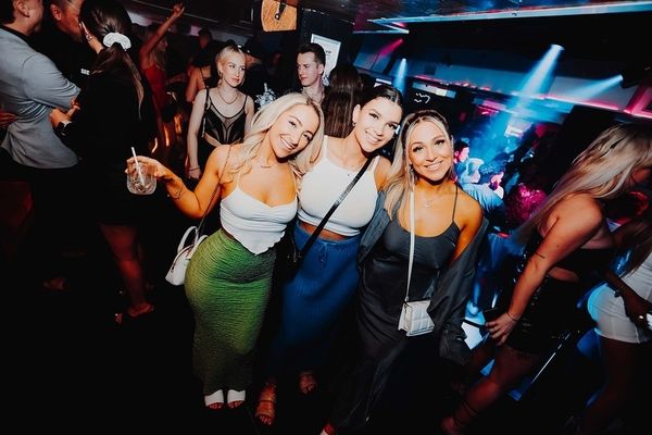 Three smiling friends posing together on a busy dance floor