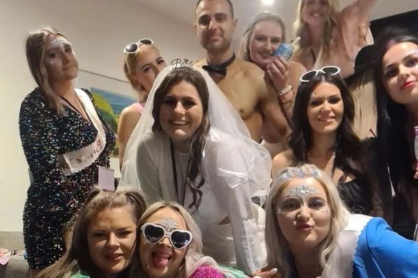 Hens group in heart sunglasses around the bride in a veil, shirtless waiter behind