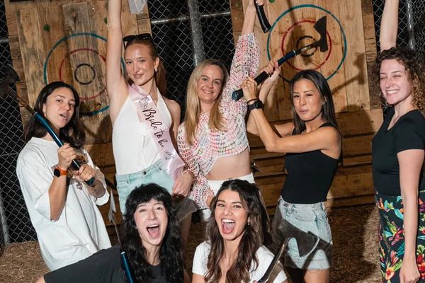 Hens group with axes raised, laughing in front of wooden axe throwing targets