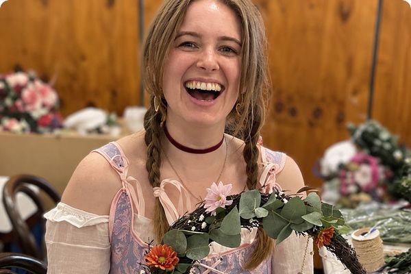 A laughing guest in plaits holds up her finished crescent moon wreath