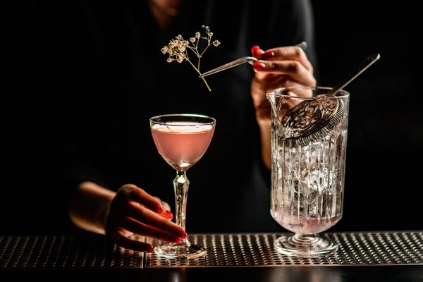 The bartender demonstrates how to add toppings to a cocktail drink during cocktail making class