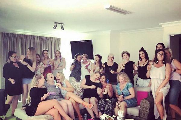 Large group of women laughing and holding drinks together in a lounge room