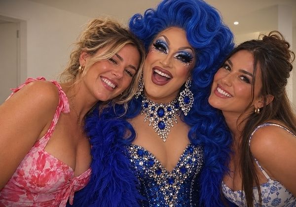 Two friends posing with a drag queen in a blue wig and sparkling gown