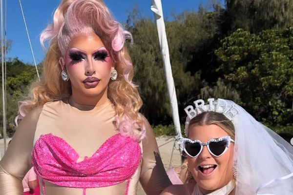 Drag queen in pink sequins beside the bride in a veil and heart sunglasses