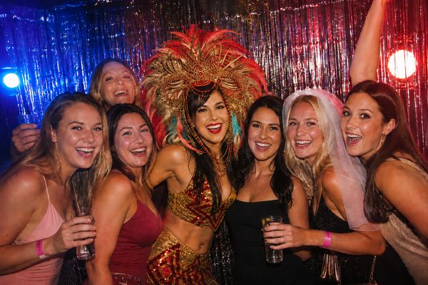 Laughing friends posing with a showgirl in a feather headdress in front of a tinsel curtain