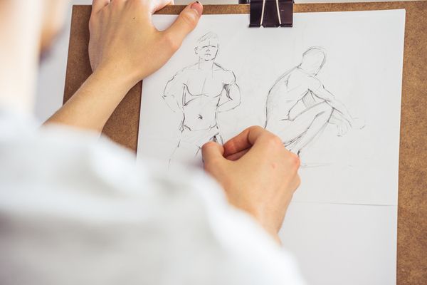 A hand sketching a male model at a life drawing class